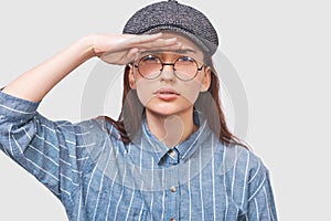 Closeup studio portrait of Caucasian young woman posing for advertisement wearing blue shirt, gray cap and round transparent