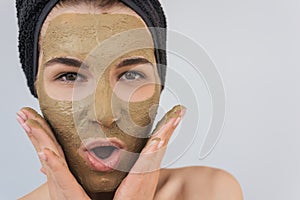 Closeup studio portrait of happy amazed young woman applying facial cosmetic clay organic mask on her face, wears black towel on