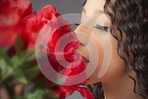 Closeup studio portrait of young Latina woman smelling red flowers