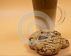 Closeup studio shot of three layered tea drink and chocolate chip cookies with orange background