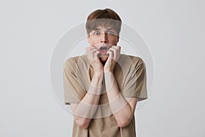 Closeup of stunned scared young man with opened mouth wears beige t shirt standing and shouting  over white background