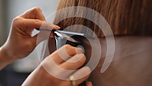 Closeup styling even line of hair with clipper in slow motion. Close-up female Caucasian hands cutting endings of hairdo