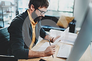 Closeup of stylish bearded designer in eye glasses working at sunny loft studio.Man using contemporary desktop computer