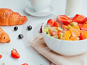 Closeup summer breakfast with bowl of healthy fresh fruit salad, coffee, milk and croissants