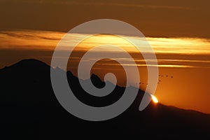 Closeup of sun rising over Mt. Baker in Washington with clouds and birds