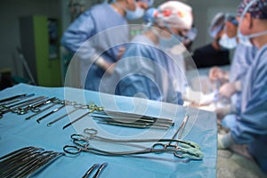Closeup of surgical tools on table and team of surgery doctors operating a patient in hospital room