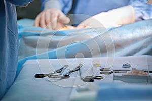 Closeup of surgical tools on table and team of surgery doctors operating a patient in hospital room