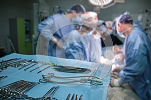 Closeup of surgical tools on table and team of surgery doctors operating a patient in hospital room