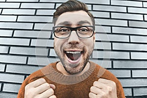 Closeup surprised man in eyeglasses looking at camera and open mouth on brick background