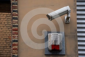 Closeup of a surveillance camera on a beige wall of a brick building