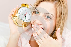 Closeup on sweet cute charming young woman blond girl with sleepy face and an alarm clock in hand