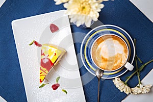 Closeup on sweet dessert piece of cake with yellow icing and red sauce with a cup of cappuccino coffee