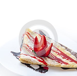 Closeup of sweet french crepes with chocolate and strawberry syrup on restaurant plate. Sweet dessert food with fruit and carame