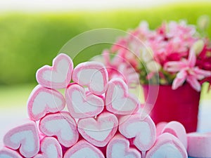 Closeup of sweet marshmallow in the shape of heart on wooden plate and flower at background.