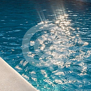 Closeup of swimingpool with clean blue water and sun rays summer background