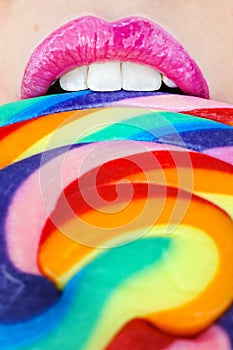 A closeup of a swirl rainbow lollipop and pink lips