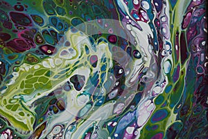 Closeup of a swirling abstract acrylic pour painting with blending greens, blues, and purples.