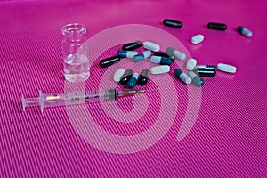 Closeup of a syringe needle with an ampoule and pills on a pink background