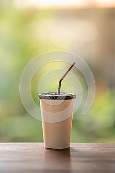 Closeup of take away paper cup of iced coffee on wooden table with green nature background