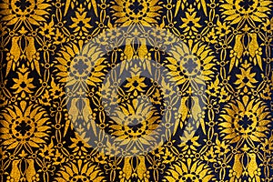 A Closeup of a tapestry or fabric patern in gold and black with flowers and birds background backgrop