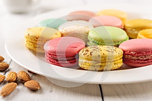 Closeup of tasty multicolored macaroons on a white porcelain plate. Sweet breakfast with delicious almond meringue cookies.