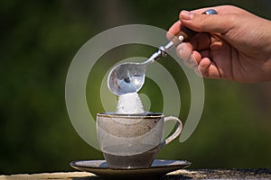 Closeup of a teaspoon of sugar being poured into a cup of hot black coffee