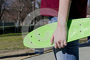 Closeup of teenage girl holding a green penny skateboard waiting to restart her skating activity