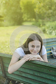 Closeup of teenage girl sitting, relaxing in the park, on a bench. Education, school girl. Smiling young woman. Summer time,