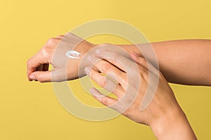 Closeup of tender hands of a young woman with moisturizer on against yellow background. spring skin protection