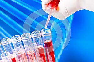 Closeup of test tubes with pipette on red liquid on abstract dna background