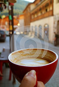 Closeup Texture of Half Cup of Hot Cappuccino Coffee in Woman`s Hand against Blurry Old Town