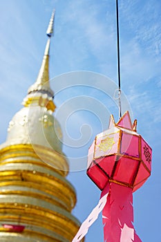 Closeup Thai Lanna style lanterns to hang in front of the golden pagoda at Thai temple under blue sky background