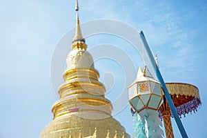 Closeup Thai Lanna style lanterns to hang in front of the golden pagoda at Thai temple under blue sky background