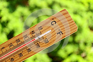 Closeup a thermometer showing high temperature against green trees in summer sunlight