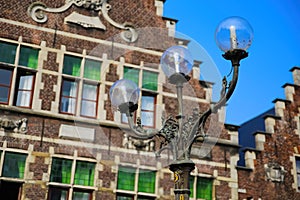 Closeup of three armed old street lamp with typical belgian stepped gable house facade background against blue sky