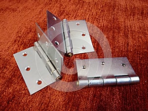 Closeup of three chrome door hinges on a red surface