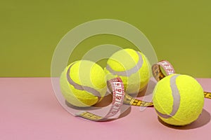 Closeup of three tennis balls,yellow measuring tape on the pink surface against green background.Empty space