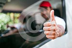 Closeup of thumb-up of a blur happy male professional truck driver from the truck window before delivering the parcel.