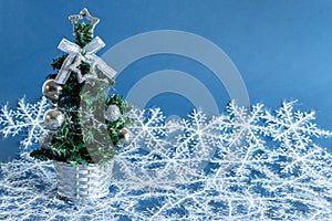 Closeup of a tiny Christmas tree with ornaments on a blue surface with snowflakes on it