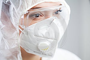 Closeup of tired female doctor,nurse or lab tech wearing PPE protective suit,white face mask and goggles