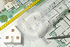 Closeup to floor plans, white paper house and measuring yellow tape. Architect drawings, expensive renovation,  buildings