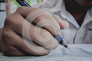 Closeup to hand of student holding pen and taking exam in classroom with stress for education test.