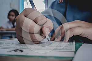 Closeup to hand of student holding pen and taking exam in classroom with stress for education test.