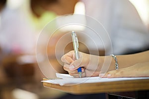 Closeup to hand of student holding pen and taking exam in classroom with stress for education test