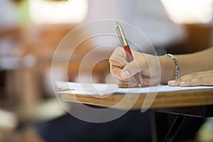 Closeup to hand of student  holding pen and taking exam in classroom with stress for education test