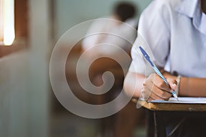 Closeup to hand of student  holding pen and taking exam in classroom with stress for education test