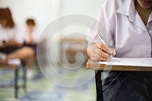 Closeup to hand of student  holding pen and taking exam in classroom with stress for education test