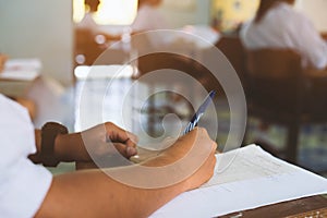 Closeup to hand of student  holding pen and taking exam in classroom with stress for education test