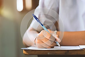 Closeup to hand of student  holding pen and taking exam in classroom with stress for education test