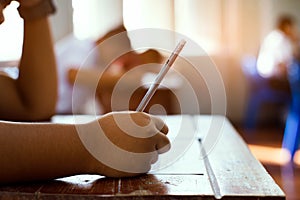 Closeup to hand of student  holding pencil and taking exam in classroom with stress for education test